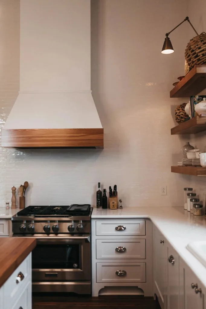 Minimalist kitchen with wood hood and white cabinetry, courtesy of a cabinetry supply business..